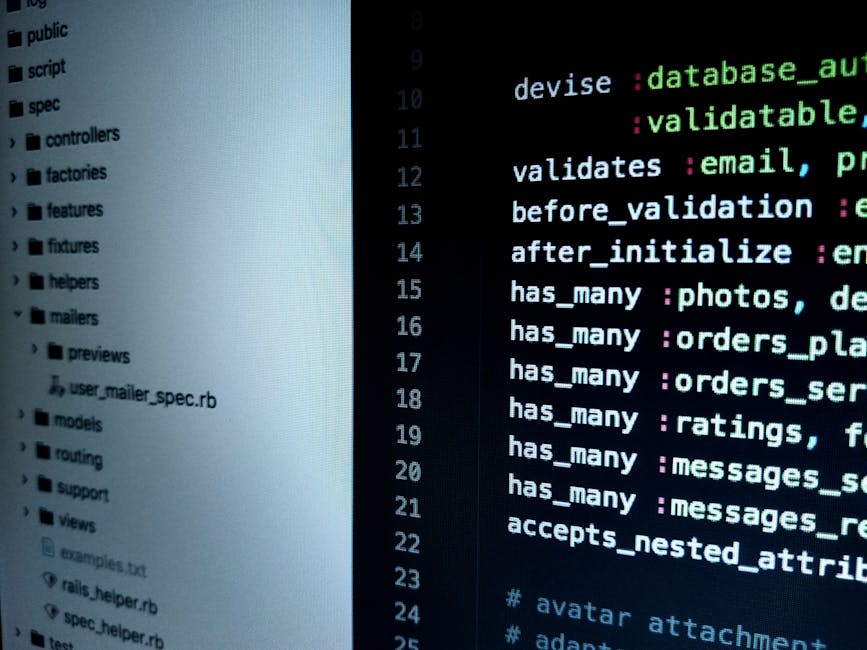 A close-up image showing a laptop open on a wooden desk, displaying lines of code on its screen with syntax highlighting in green, blue, and red text. The laptop's metallic keyboard is visible in the 
